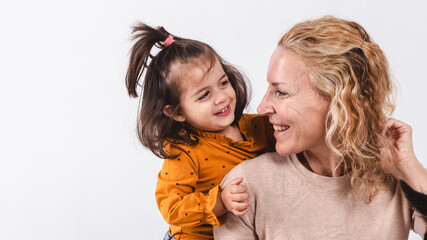 Portrait of a woman and her daughter looking at each other smiling in a studio shot on a white background.