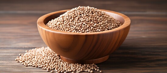 A wooden bowl filled with seeds, specifically raw buckwheat grain, sits atop a wooden table. The grains are neatly arranged, creating a simple yet rustic composition.