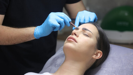 Obraz na płótnie Canvas A cosmetologist marks with a pen the site of a beauty injection in the forehead of a beautiful patient. Concept of preparing for an injection of a beautiful young woman.