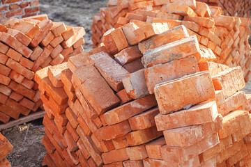 Obraz na płótnie Canvas Stack of red bricks, process of house building. Bricks for laying on concrete foundation. Building materials at construction site