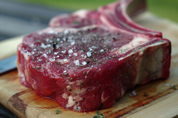 Premium Raw Tomahawk Steak Seasoned with Coarse Salt and Herbs on a Wooden Cutting Board