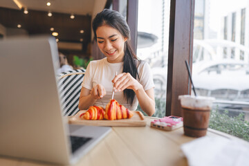 Happy smile asian woman eating bread at cafe sitting near window indoors on day