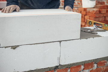 Builder installing masonry white blocks close up. Worker laying autoclaved aerated concrete blocks. Process of house building at construction site