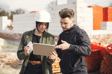 Stylish woman architect with tablet  and contractor man checking blueprints at construction site....
