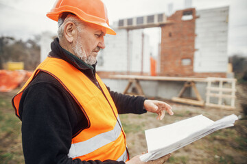 Senior man engineer or construction worker in hardhat looking at blueprints at building new modern...