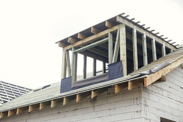 Unfinished house. Wooden roof framing with vapor barrier and dormer on block walls with windows....