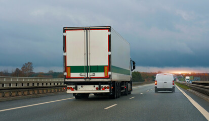 White semi-trailer trucks on the highway driving in the left lane. Commercial vehicle for shipping...