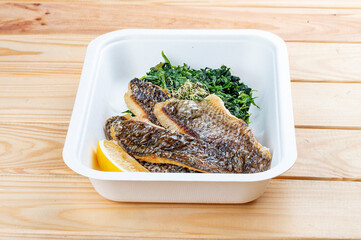 Sea bass fillet with spinach. Healthy food. Takeaway food. On a wooden background.