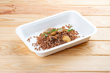 Buckwheat porridge with mushrooms. Healthy food. Takeaway food.  On a wooden background.