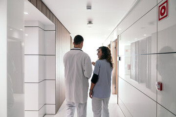 Rear view of healthcare workers in dialogue in hospital corridor.