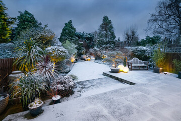 Beautiful English designer garden and patio with garden lighting in snow.