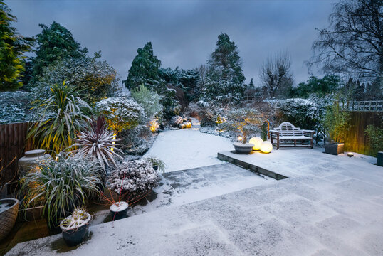 Beautiful English designer garden and patio with garden lighting in snow.
