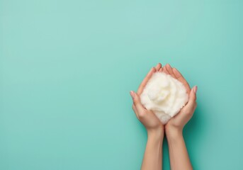 Womans hands cradles a mound of fluffy white soap foam against a turquoise background - obrazy, fototapety, plakaty