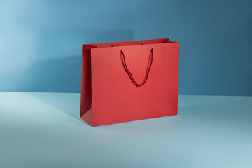 Red paper glossy shopping bag mockup with red handles on blue background.