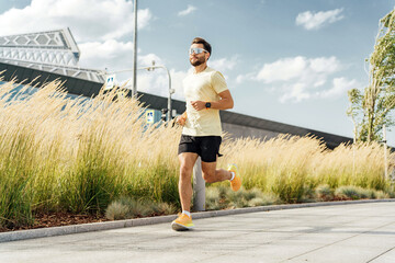 Man running in urban park with tall grass and modern architecture.