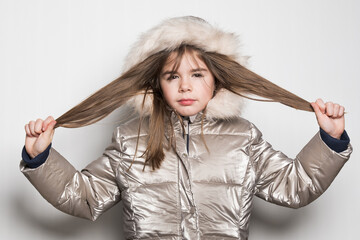 Une petite fille de 7 ans avec un blouson brillant d'hiver qui se tient les cheveux - 747153501
