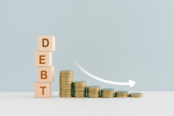 DEBT word on wooden cube blocks word and down arrow with stack of coin for financial debt decrease...
