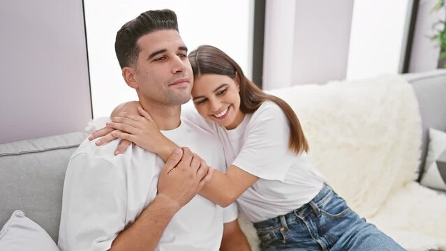 A smiling woman embraces a man on a cozy sofa in a modern living room, depicting love and togetherness.