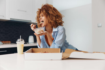 Woman eating cereal in front of pizza box at breakfast time in cozy kitchen environment