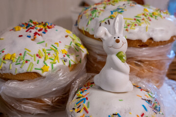 white easter rabbit standing on home-baked easter cakes with icing on a table in the kitchen....