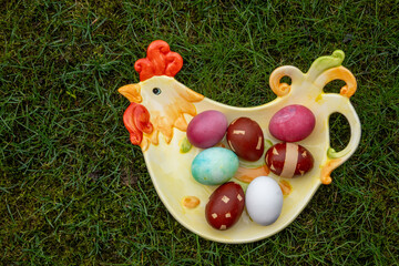 dyed easter eggs on the chicken-shaped plate on green background. Easter celebration