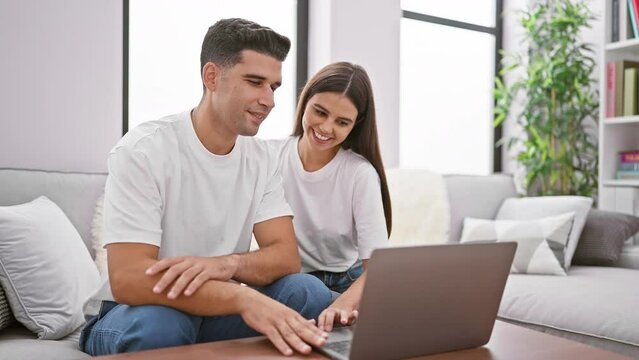 A smiling couple using a laptop together in a modern living room, depicting intimacy and technology in a home setting.