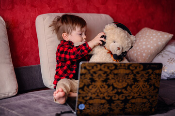 A delighted young child hugs a teddy bear while engaging with a laptop, a scene merging the comfort...