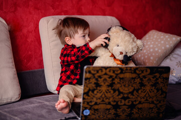 A delighted young child hugs a teddy bear while engaging with a laptop, a scene merging the comfort...