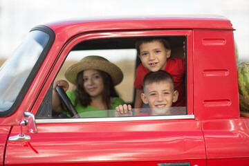 three children siblings  sit in the cab of a red pickup truck with watermelons.  summer time in...