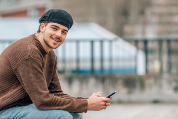 portrait of young man with mobile phone outdoors on the street wearing urban style cap