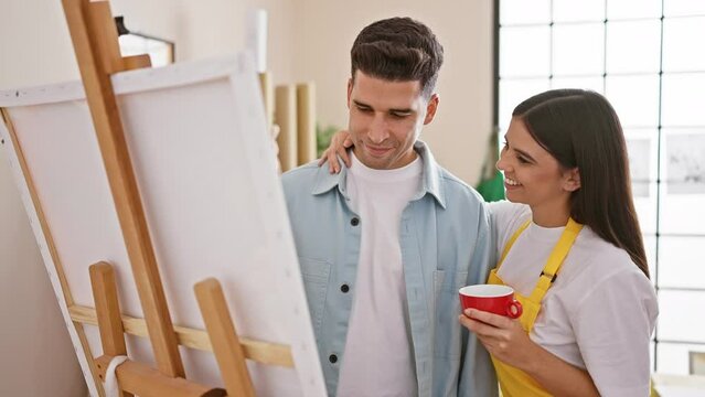 A man and a woman, appearing as a couple or artists, share a tender moment in a bright art studio.
