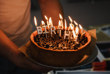 Burning candles with the words "Happy Birthday". Man hold birthday cake. Celebration birthday cake with silver candles spelling happy birthday on party. Closeup.