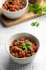 Food dish made of beans, tomatoes, and cilantro on a wooden table