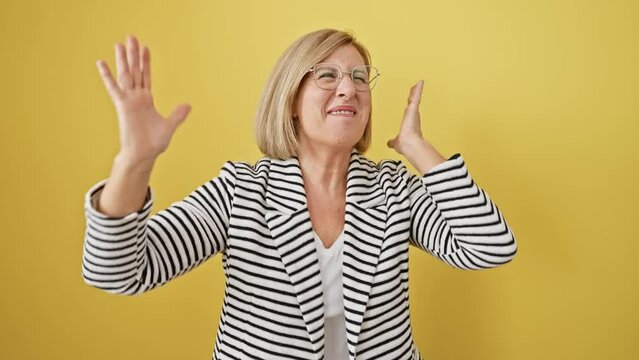 Cheerful, blonde, middle-aged woman in a striped jacket, ecstatically cheers her win! she's standing, exulting in victory, amidst a bright yellow isolated backdrop.
