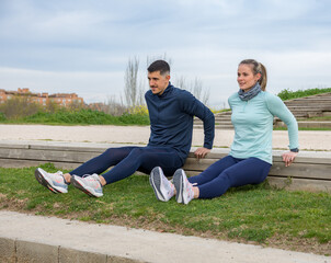 Lower couple young two friend strong sporty sportswoman sportsman woman man in sport clothes warm up training do stretch exercise outdoors in a park.