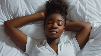 A young woman with closed eyes lying on her back on a white bed wearing a white blouse with her arms resting on her head appearing relaxed and at peace. - 747185311