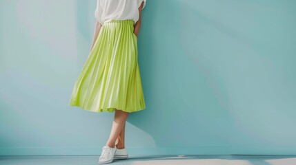 A woman in a vibrant lime green midi skirt and white top standing against a light blue wall with her legs crossed and hands resting on her hips exuding a casual yet chic style.