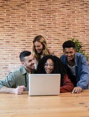 Diverse group of young adult friends working sharing a computer in a modern apartment. University students using laptop together.