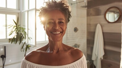 A woman with a radiant smile standing in a well-lit bathroom with a window and a potted plant in the background.
