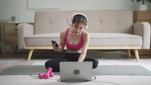 athlete asian woman wearing headphone using smartphone at her home
