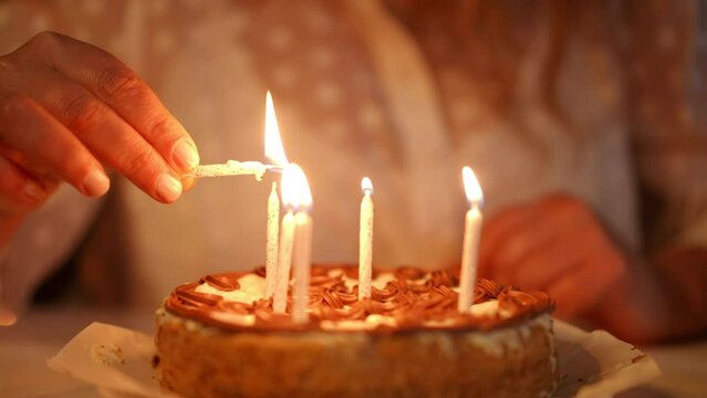 Close-up. An unrecognizable woman lights candles on a birthday cake while sitting at the table