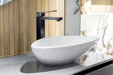 A sleek modern bathroom featuring a white vessel sink paired with a stylish black faucet, set against wood and marble textures.