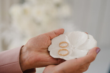 Engagement. Two golden wedding rings are on a white plate in hands woman. Top view.