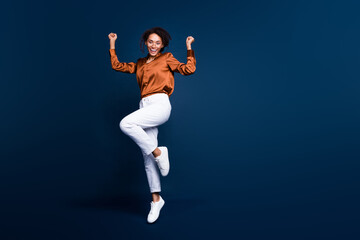 Full length photo of lovely young lady jump excited winner dressed stylish brown silk formalwear isolated on dark blue color background - obrazy, fototapety, plakaty