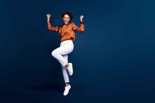 Full length photo of lovely young lady jump excited winner dressed stylish brown silk formalwear isolated on dark blue color background