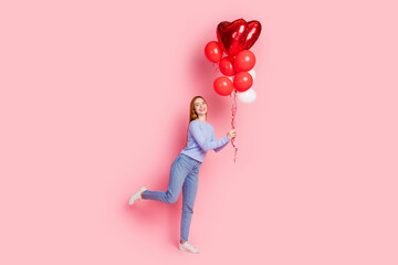 Full size photo of good mood girl wear stylish pullover jeans stand on one leg hold red balloons isolated on pink color background