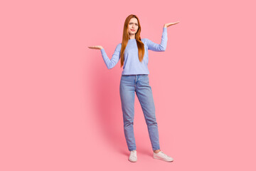 Full length photo of confused puzzled girl wear blue pullover palms hold similar objects empty space isolated on pink color background