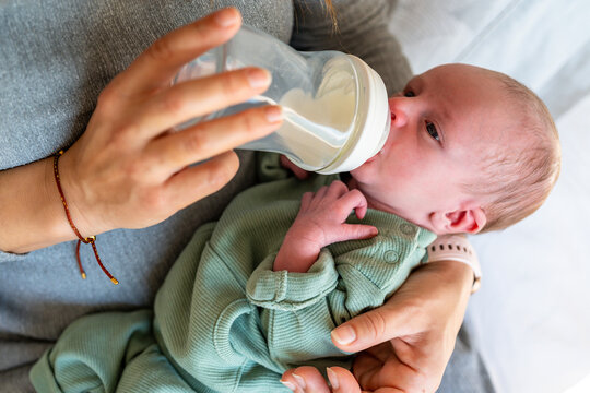 A newborn is comfortably cradled in anonymous mother's arms, being fed with a milk bottle, depicting a nurturing and caring moment