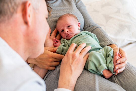 A close-up of anonymous father admiring his newborn baby, who is securely nestled in the mother's arms, displaying a tender family bond