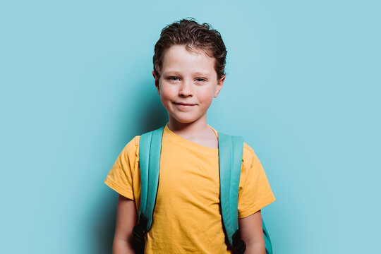 A happy young boy with a backpack smiles against a turquoise background, exuding confidence and excitement for school